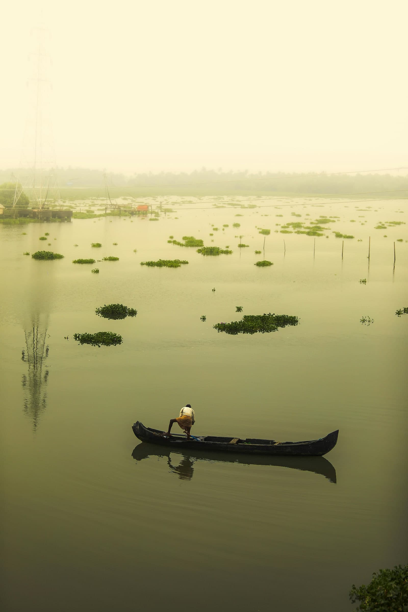A lone fisherman in a canoe on still backwater at first light